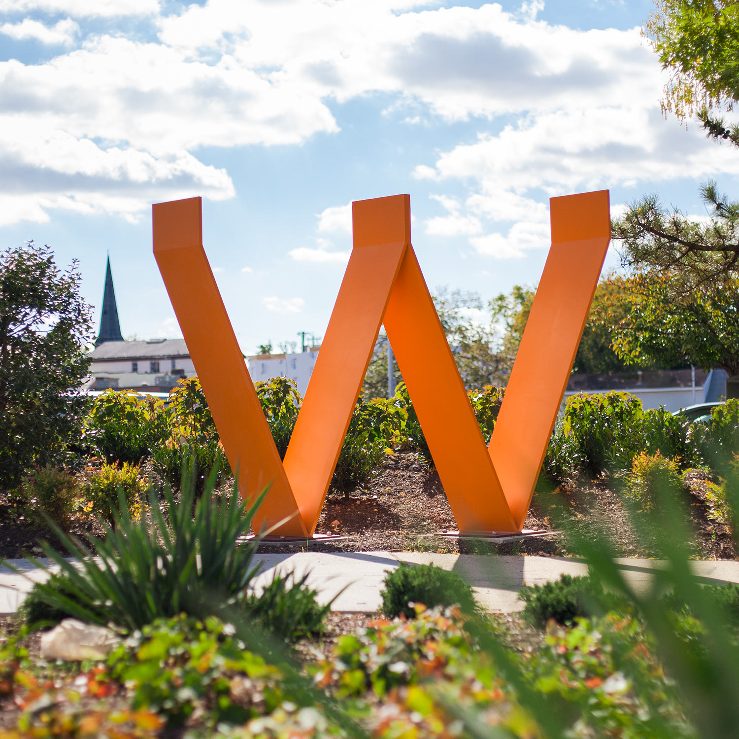 'W' sculpture surrounded by plants